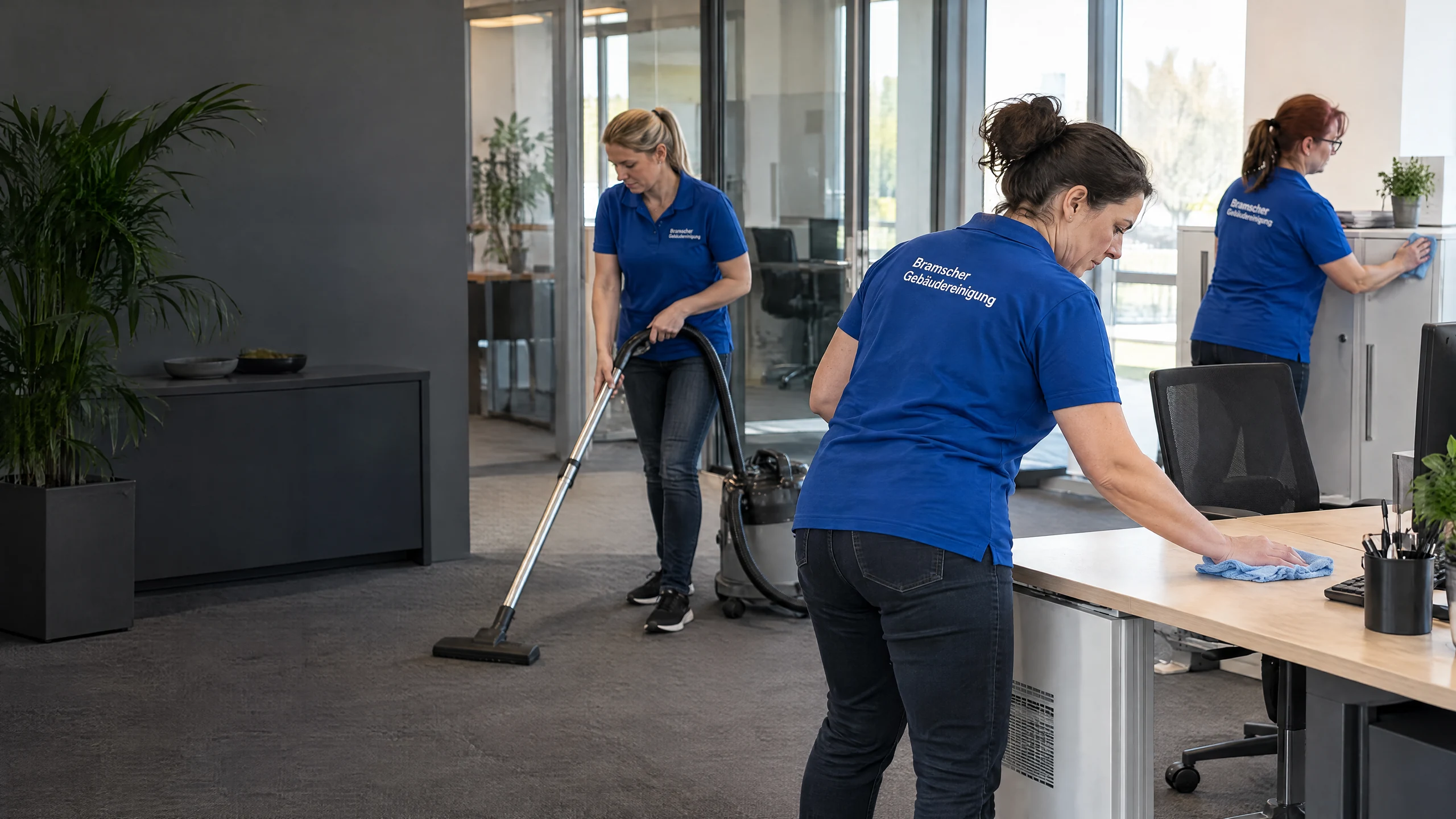 Drei Reinigungskräfte in royalblauen Bramscher-Poloshirts bei der Büroreinigung